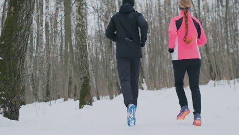 Positive-beautiful-young-healthy-couple-running-with-sportswear-through-the-forest-in-the-sunny-winter-morning.